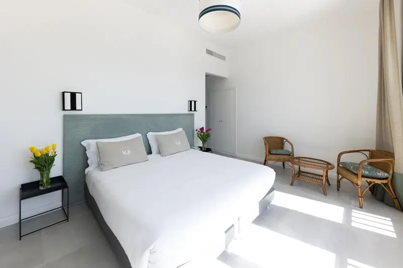 Une chambre lumineuse avec un grand lit et deux fauteuils en rotin.
