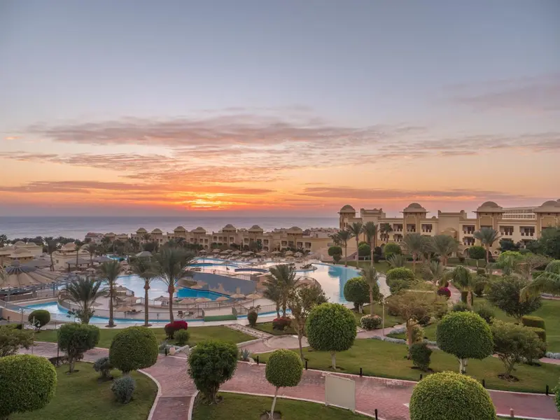 Vue aérienne d'un complexe hôtelier avec piscines et végétation luxuriante au coucher du soleil.