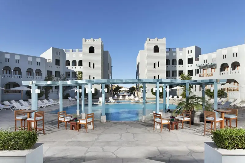 Vue d'un bâtiment blanc avec une piscine et des chaises longues.