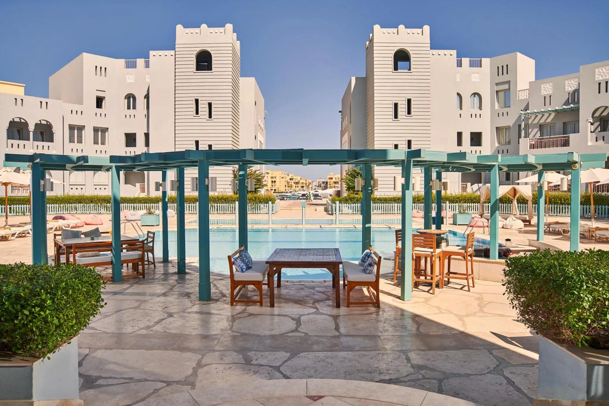 Terrasse ombragée avec tables et chaises près d'une piscine.