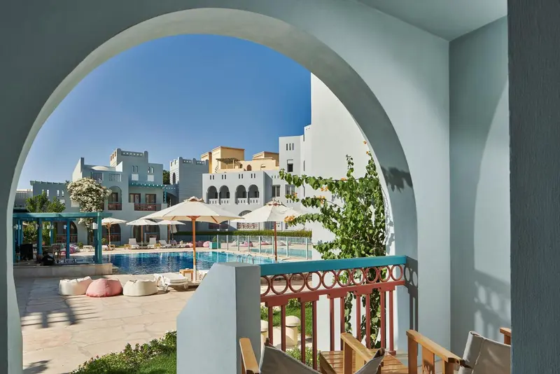 Vue sur une piscine ensoleillée depuis un balcon ombragé.