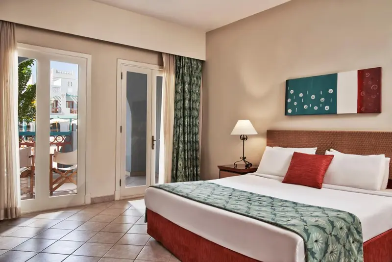 Chambre lumineuse avec un grand lit et un accès à une terrasse.