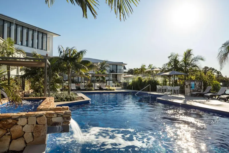 Une piscine bleue avec une cascade artificielle et des transats blancs.