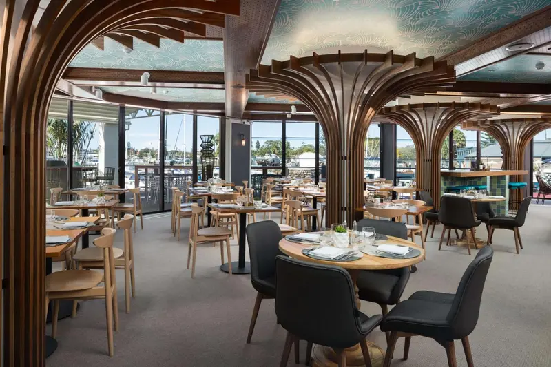 Une salle de restaurant lumineuse avec des tables dressées et une vue sur un port.