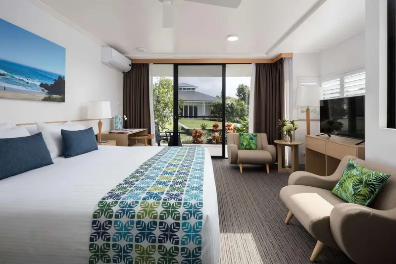 Une chambre lumineuse avec un grand lit et un coin salon donnant sur un jardin.
