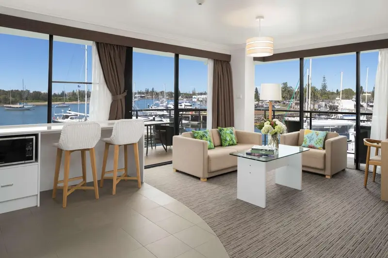 Un espace de vie lumineux avec un coin repas et un canapé face à une vue sur un port de plaisance.
