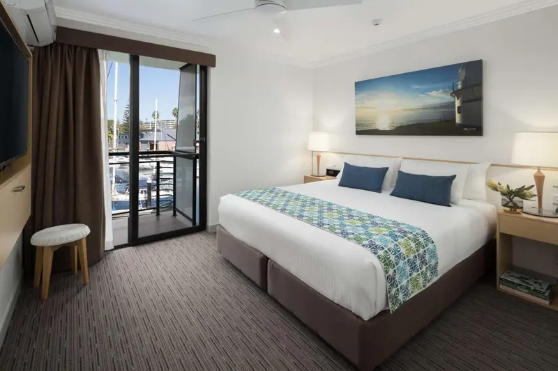 Chambre lumineuse avec un grand lit et un balcon donnant sur un port de plaisance.