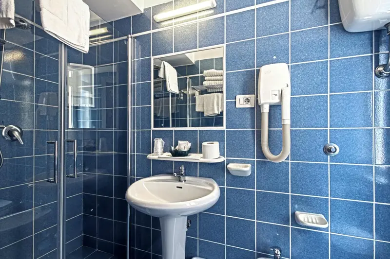 Une salle de bain carrelée de bleu avec douche, lavabo et miroir.