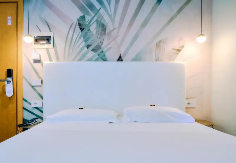 Une chambre lumineuse avec un grand lit recouvert de draps blancs et un mur décoré de motifs tropicaux.