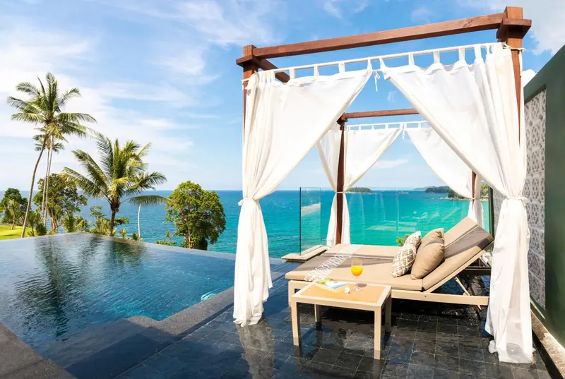Transats et pergola blancs surplombant une piscine à débordement avec vue sur la mer.