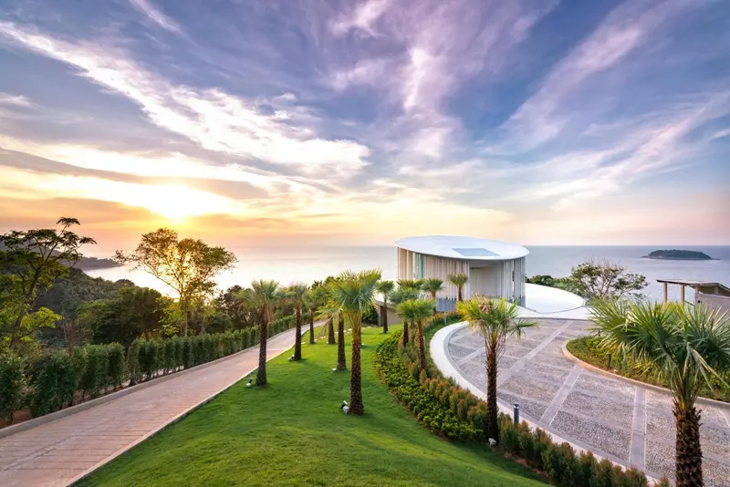 Bâtiment blanc moderne surplombant une mer calme au coucher du soleil.
