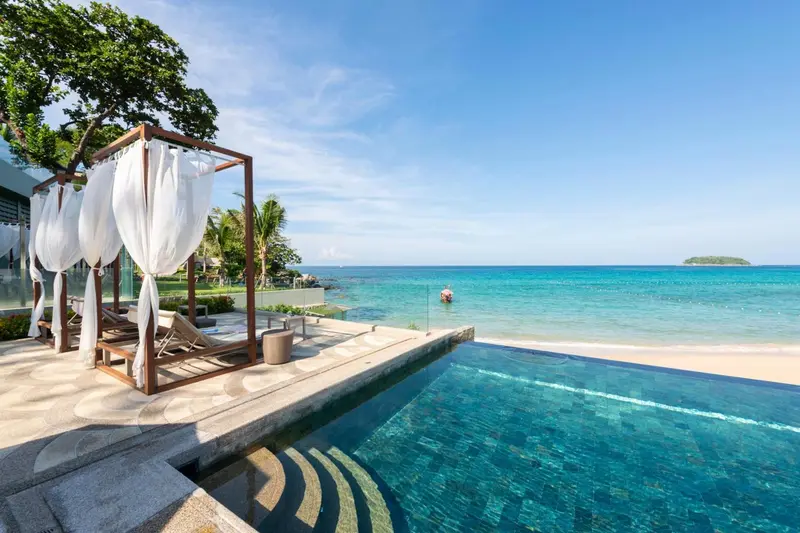 Transats et parasols blancs bordent une piscine à débordement avec vue sur la mer.