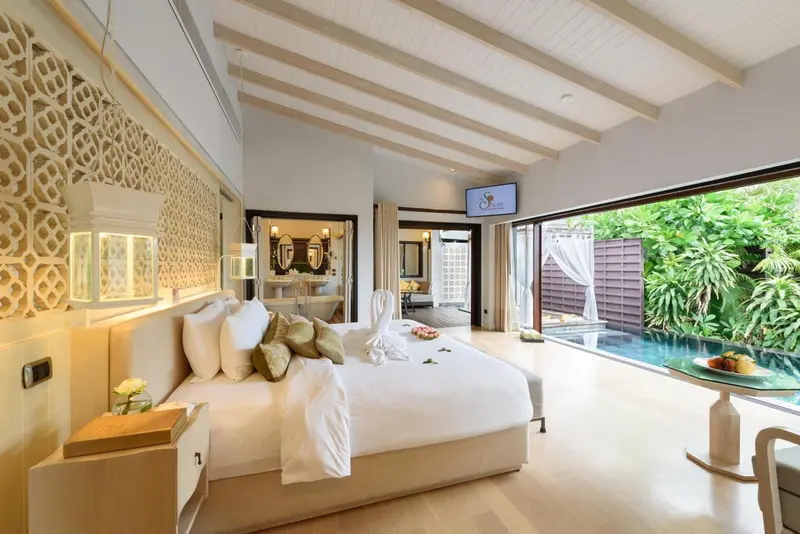Chambre lumineuse avec un lit king-size décoré de fleurs, donnant sur une piscine privée.