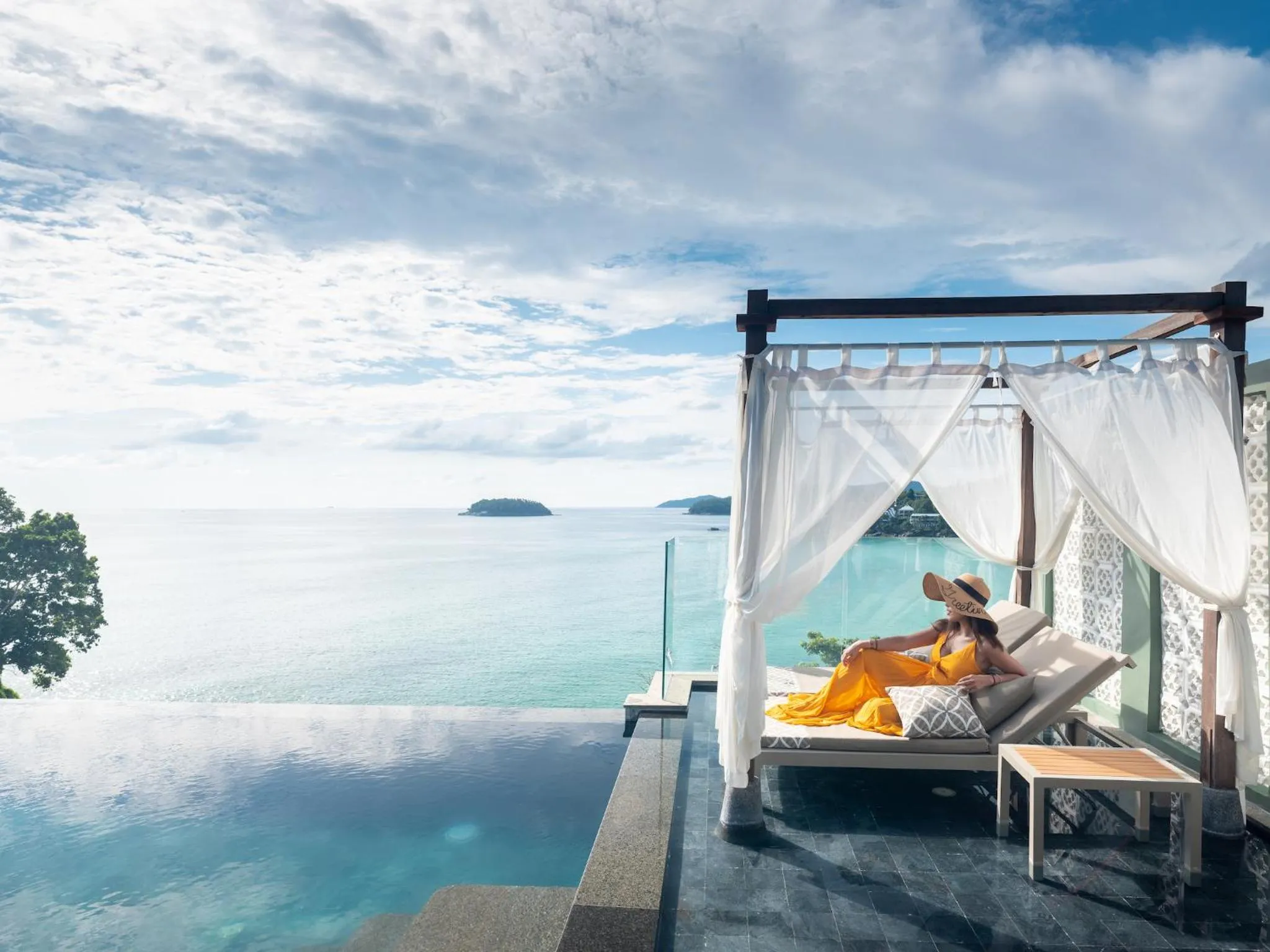 Une femme se relaxe sur des transats au bord d'une piscine à débordement avec vue sur la mer.