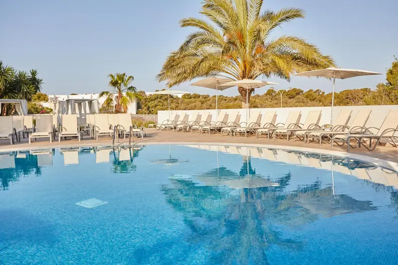 Transats alignés au bord d'une piscine turquoise sous des parasols blancs.