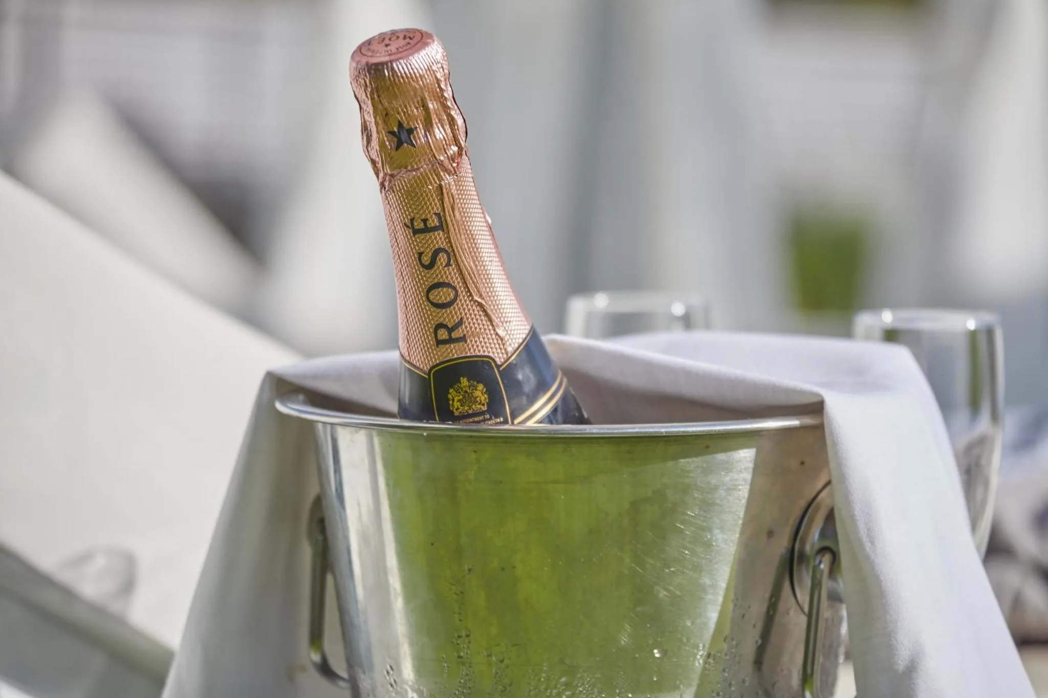 Une bouteille de champagne rosé dans un seau à glace sur une surface claire.