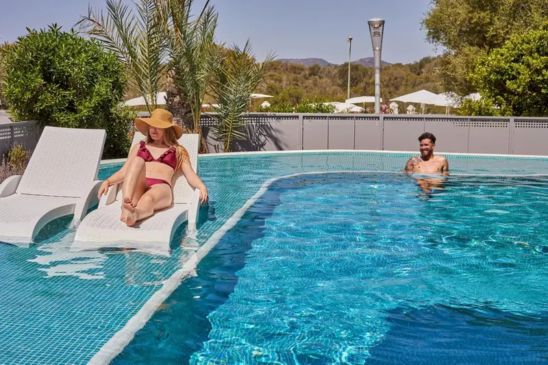 Deux personnes se relaxent au bord d'une piscine ensoleillée.