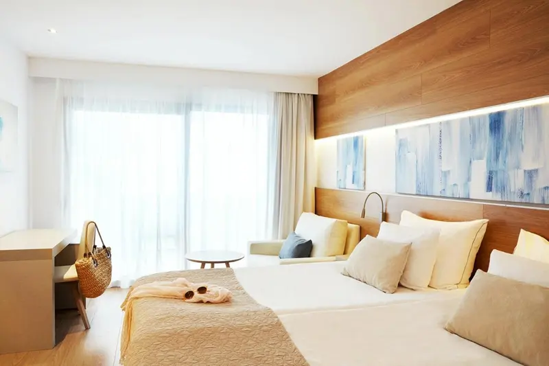 Chambre lumineuse avec un grand lit et un espace détente près de la fenêtre.