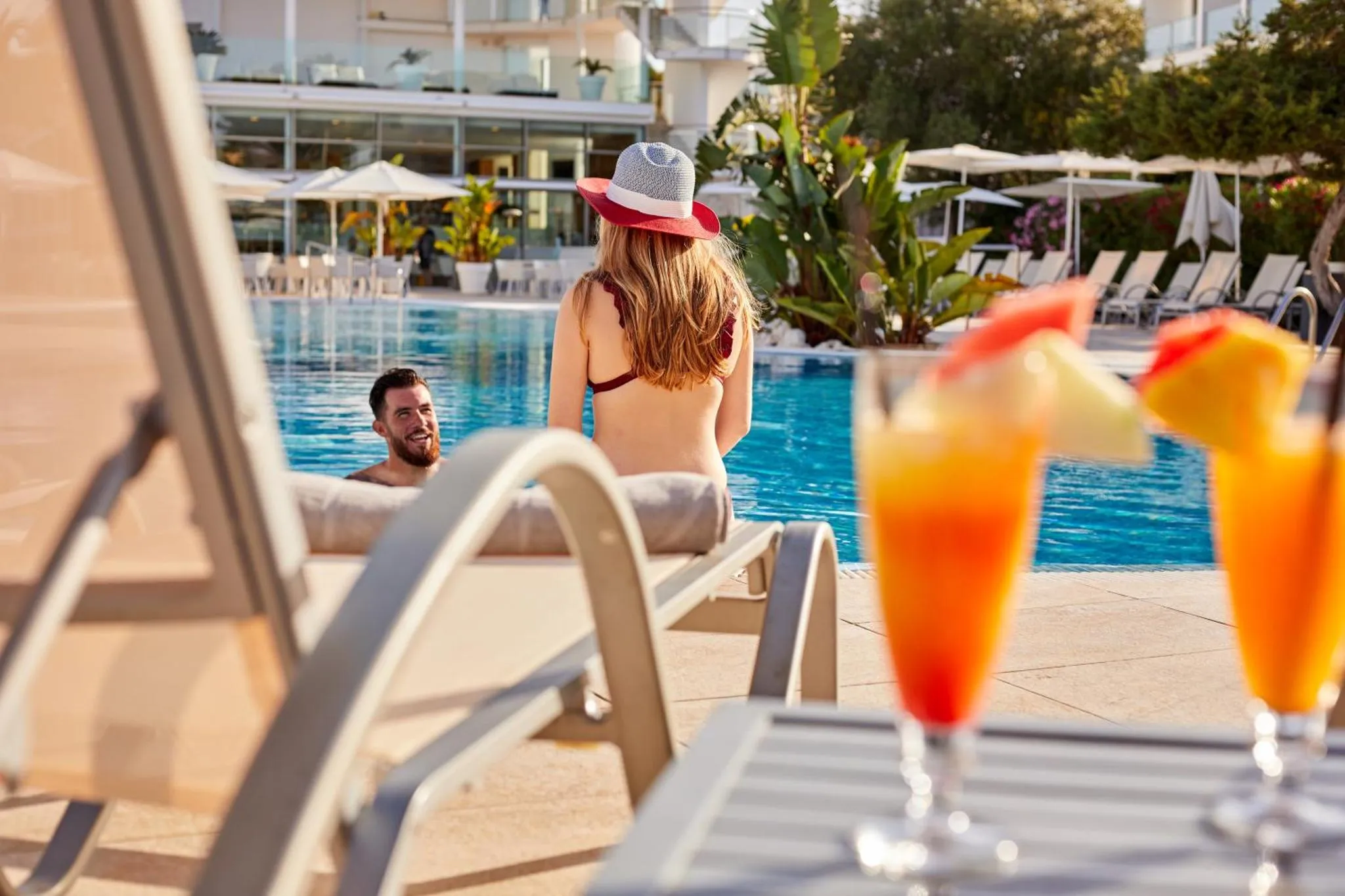 Deux transats au bord d'une piscine avec des boissons colorées au premier plan.