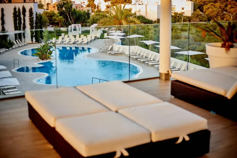 Transats blancs disposés devant une piscine bleue bordée de végétation.