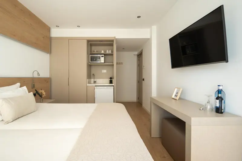 Une chambre lumineuse avec un lit fait et un espace cuisine.