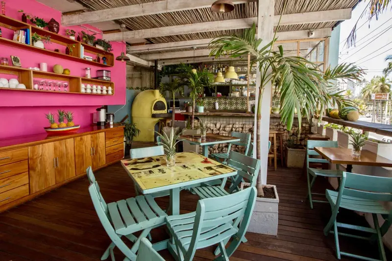Terrasse en bois avec tables et chaises turquoise, décorée de plantes et d'une étagère colorée.