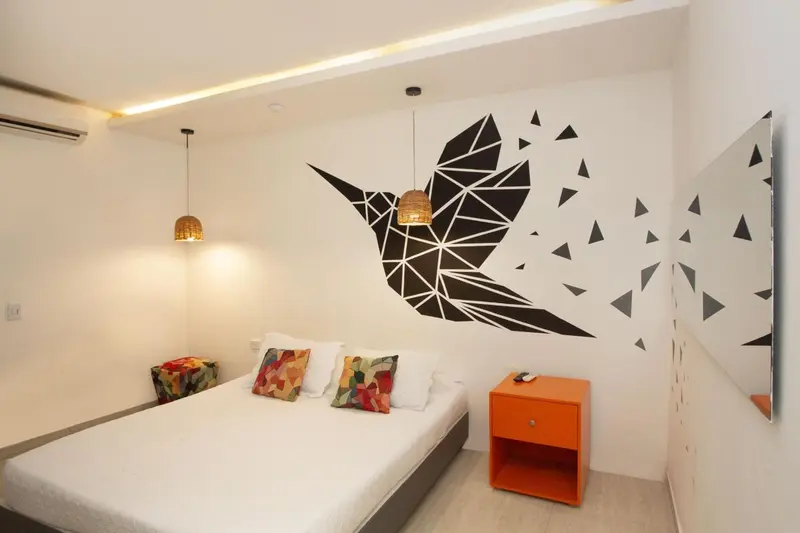 Une chambre lumineuse avec un lit recouvert de coussins colorés et une décoration murale graphique.