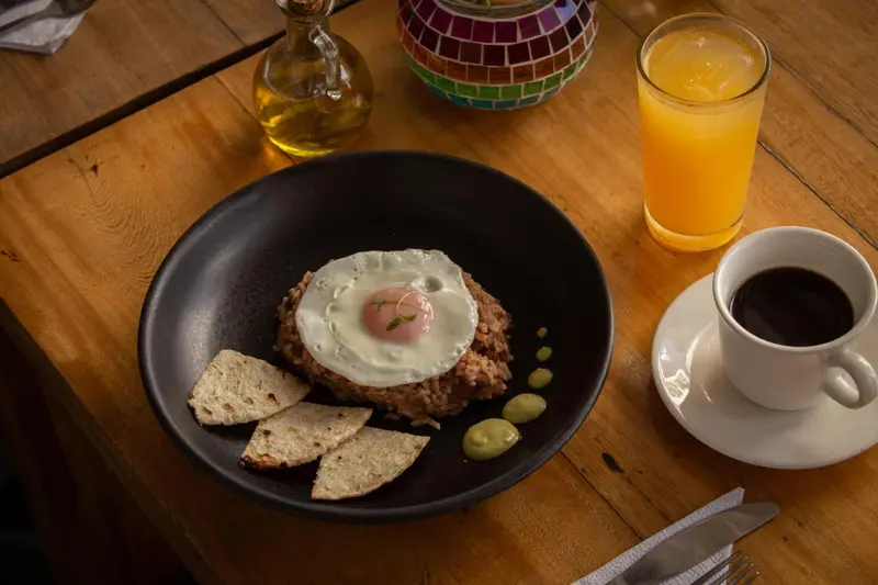 Un plat de riz avec un œuf au plat, accompagné de tortillas et d'une sauce verte, servi avec une boisson et un café.
