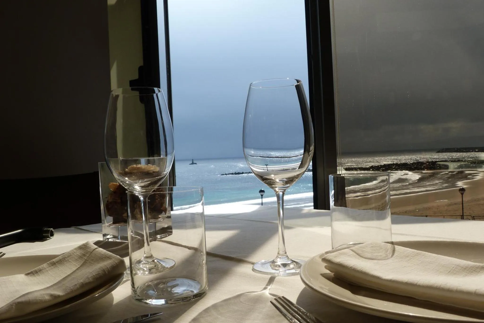 Une table dressée avec des verres et des assiettes face à une vue sur la mer.