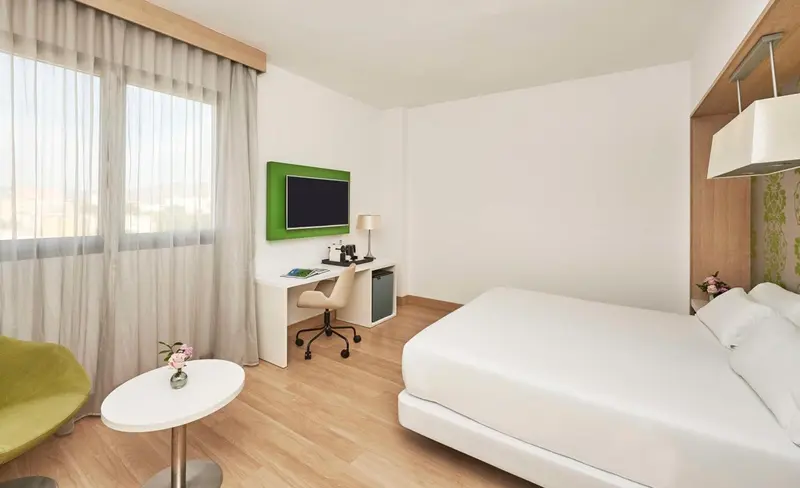 Une chambre lumineuse avec un lit blanc et un bureau près de la fenêtre.