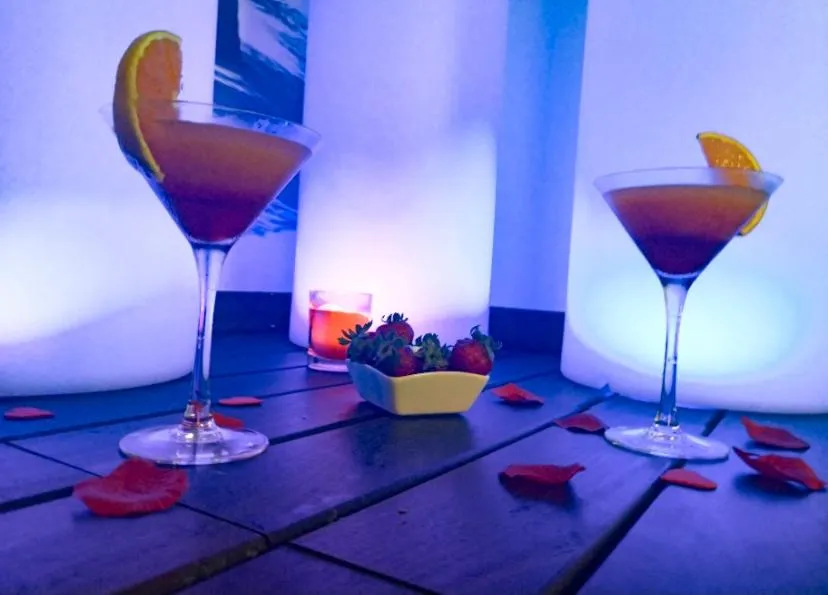 Deux cocktails colorés sont présentés avec des fraises et des pétales de fleurs sur une table sombre.
