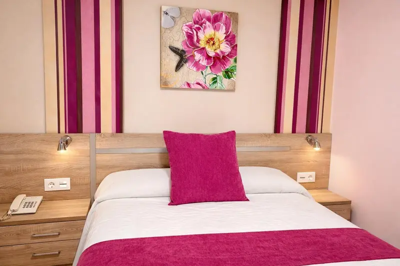 Une chambre d'hôtel avec un lit recouvert d'une courtepointe rose et d'un coussin assorti.