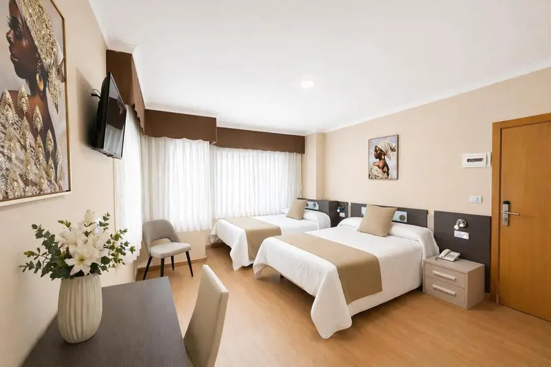 Chambre lumineuse avec deux lits simples et un espace bureau.