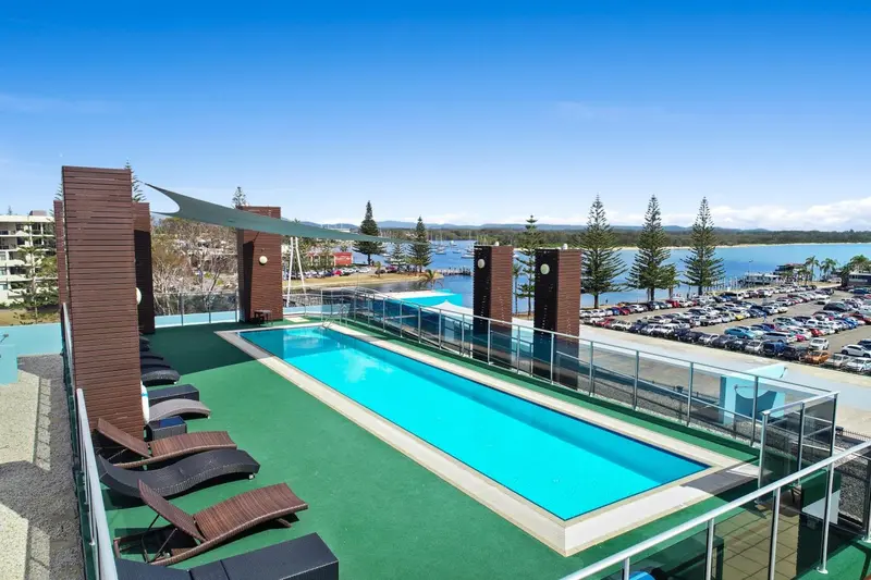 Une piscine rectangulaire sur une terrasse avec des transats et une vue sur la mer.