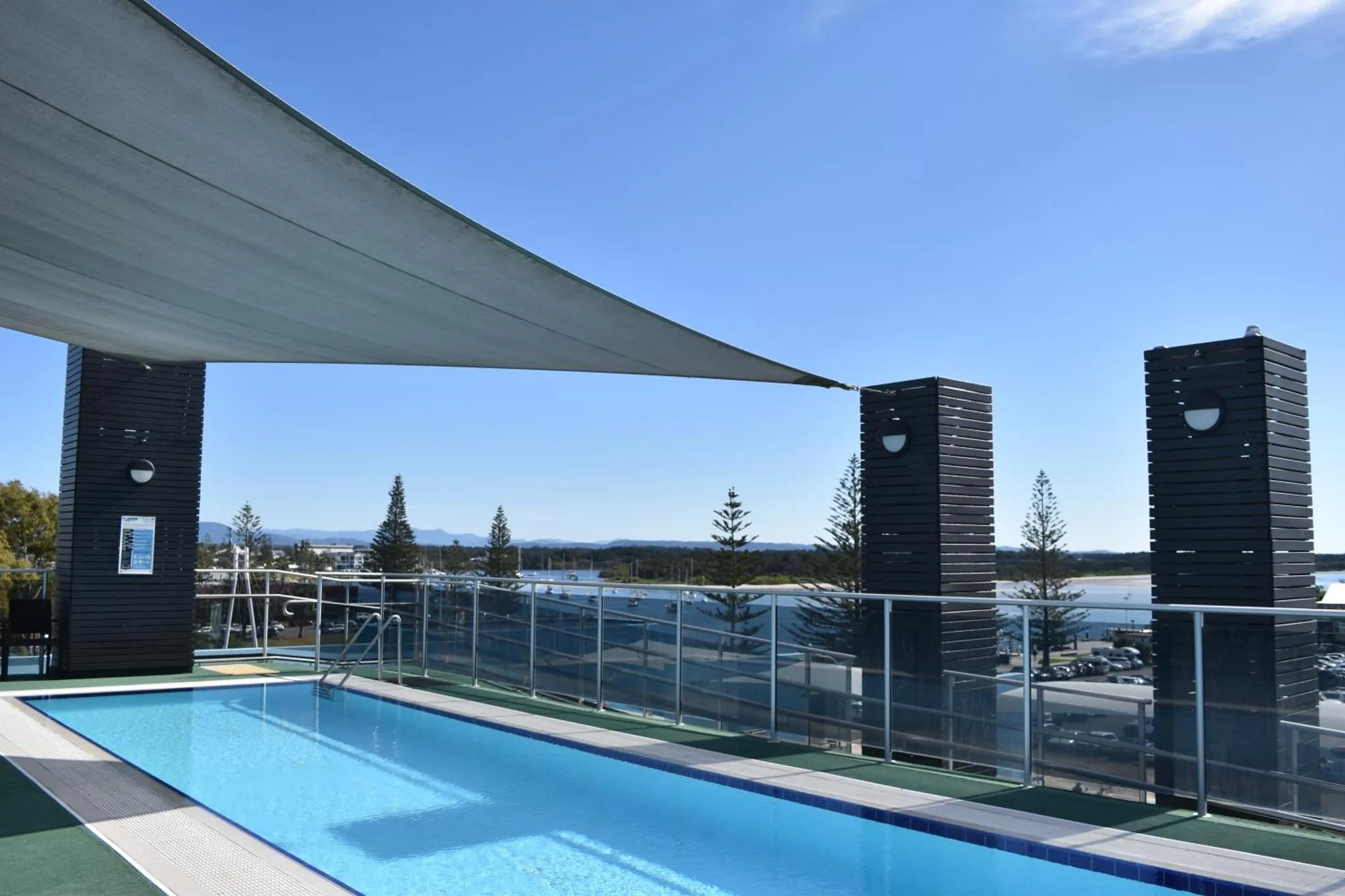 Une piscine rectangulaire avec une zone ombragée et une vue sur la mer.