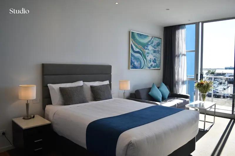 Une chambre lumineuse avec un grand lit et un canapé près d'une baie vitrée.