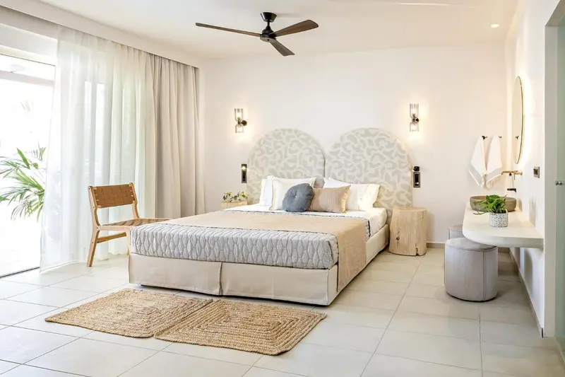 Chambre lumineuse avec un grand lit et un fauteuil en bois.