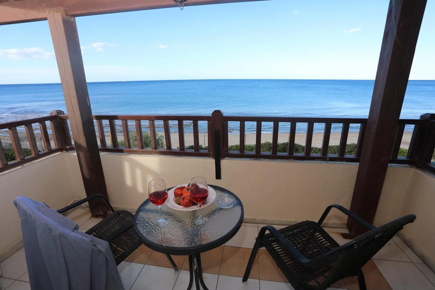 Une table ronde avec des fruits et des verres est mise en valeur sur une terrasse avec vue sur la mer.