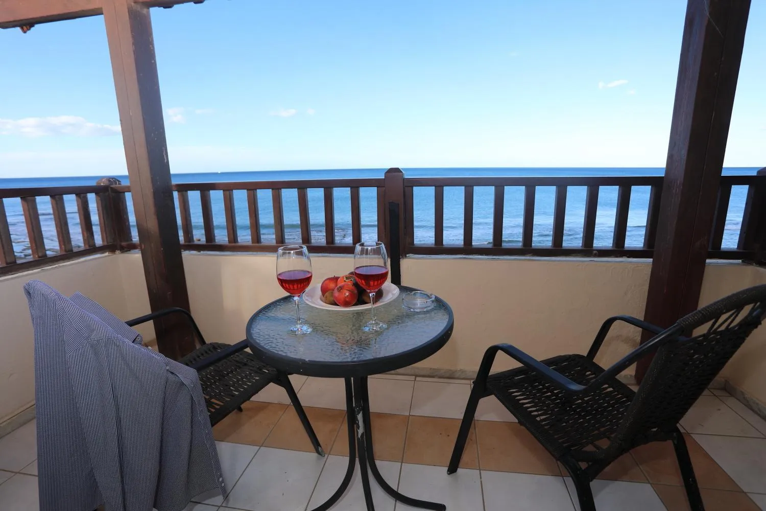 Une table avec des verres de vin et des fruits est placée sur une terrasse avec vue sur la mer.