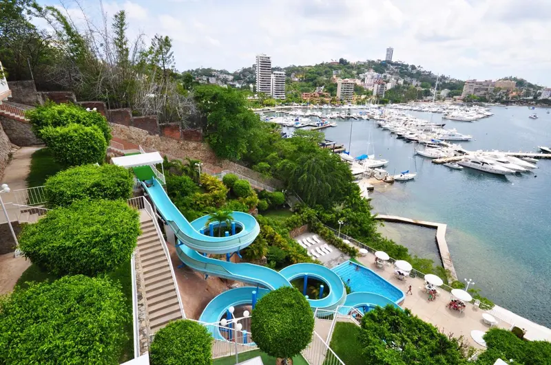 Toboggan aquatique bleu descendant vers une piscine au milieu d'une végétation luxuriante.