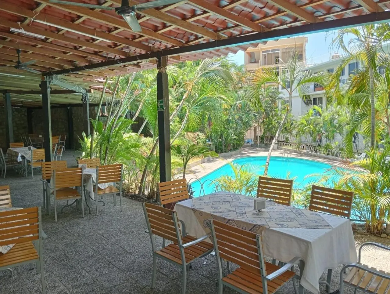 Terrasse ombragée avec tables et chaises donnant sur une piscine.