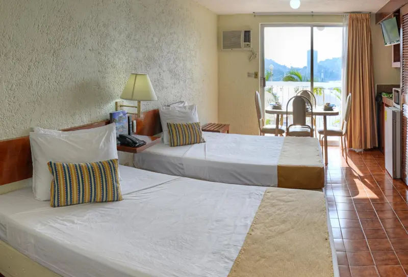 Une chambre lumineuse avec deux lits et un coin repas donnant sur une vue extérieure.