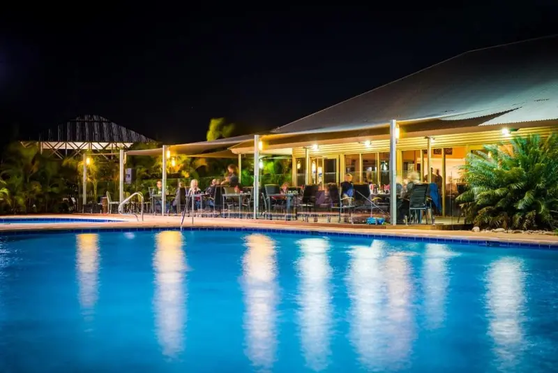 Une piscine illuminée reflète les lumières d'un bar extérieur en soirée.