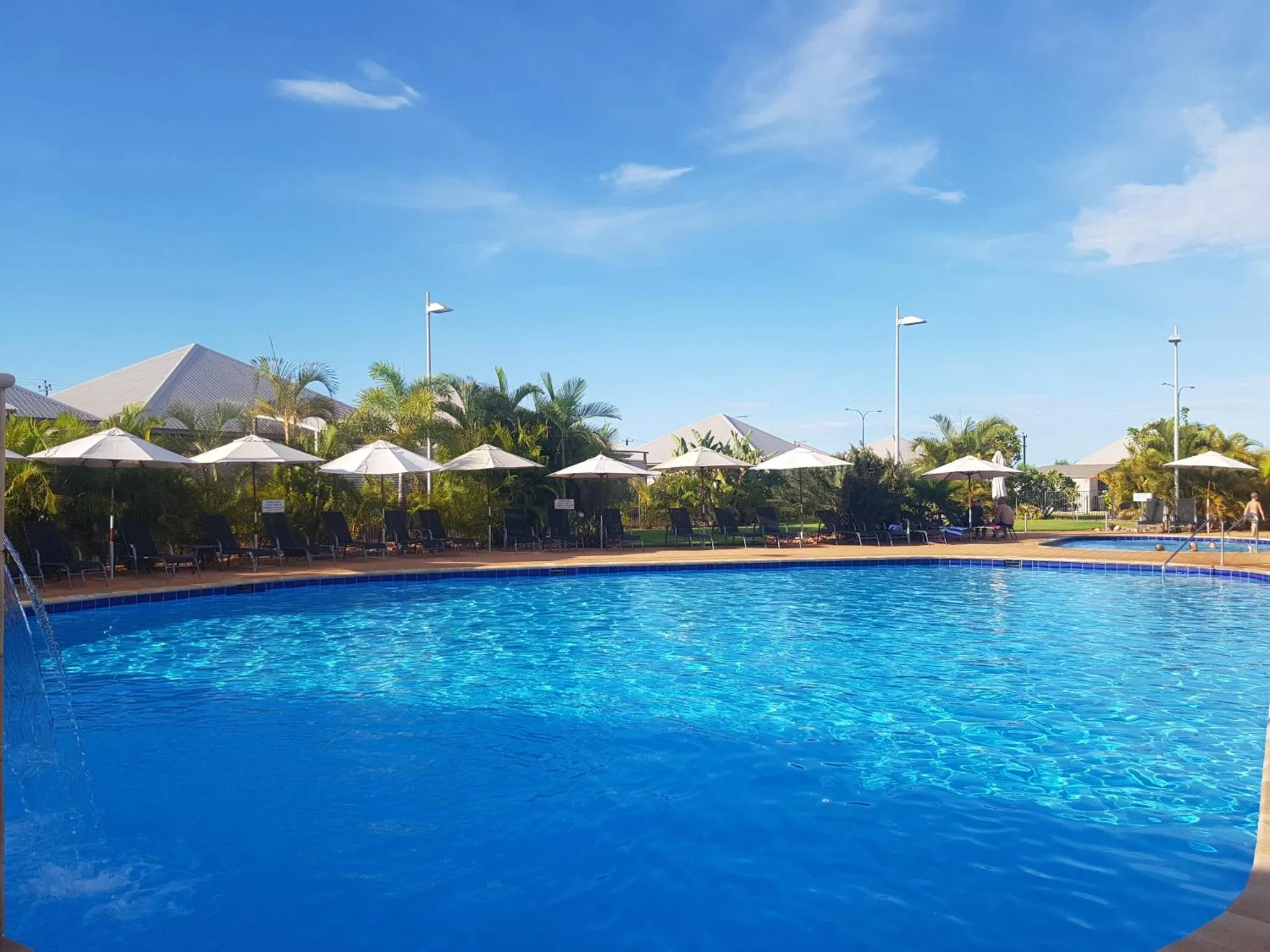 Une piscine rectangulaire bleu clair avec des transats et des parasols.