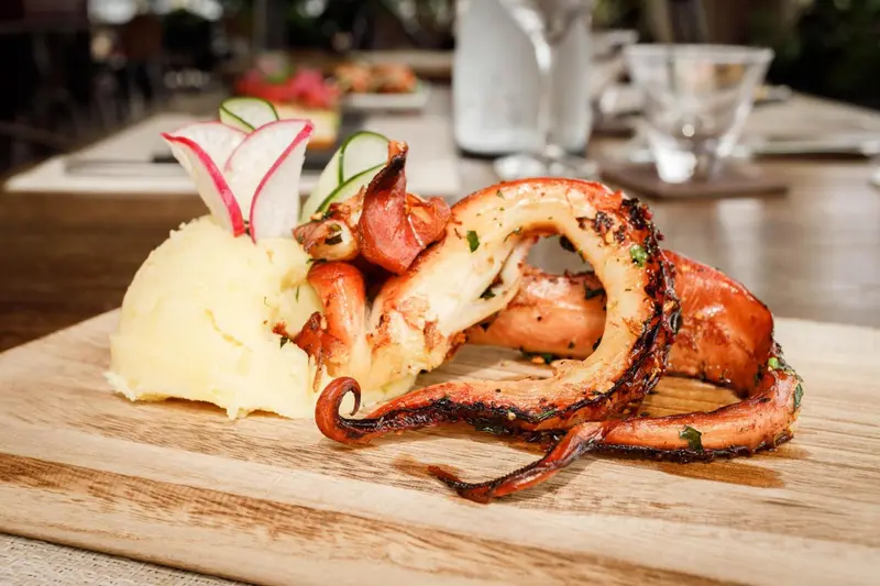 Un plat de poulpe grillé est présenté sur une planche en bois avec une purée.