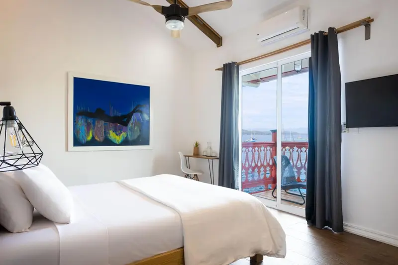 Une chambre lumineuse avec un lit blanc et un accès à une terrasse.