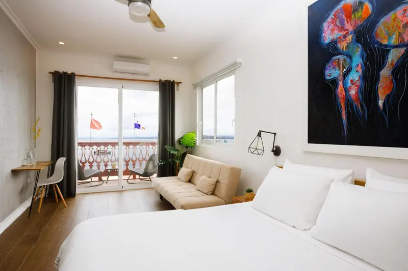 Une chambre lumineuse s'ouvre sur un balcon avec vue sur la mer.
