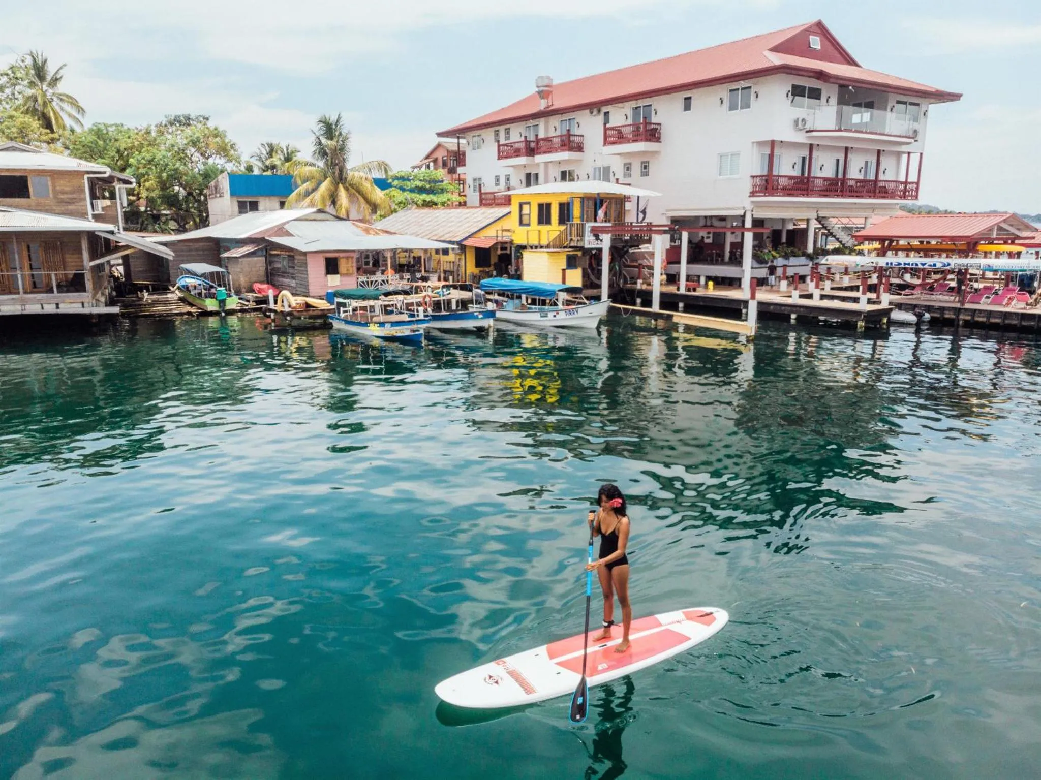 Une personne se tient debout sur une planche de paddle au milieu d'une eau turquoise.