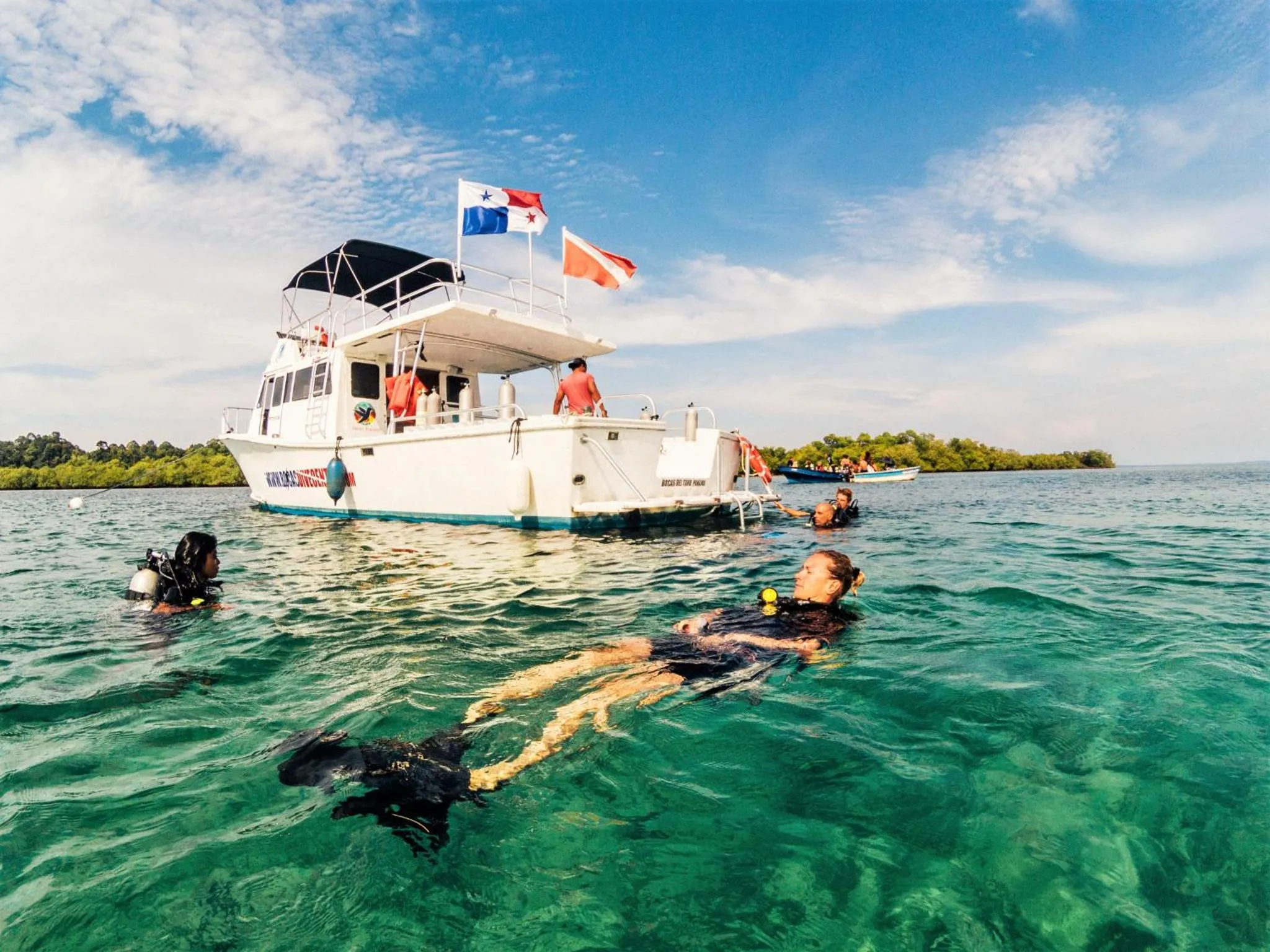 Un bateau blanc amarré sur une eau turquoise, avec des personnes nageant à proximité.