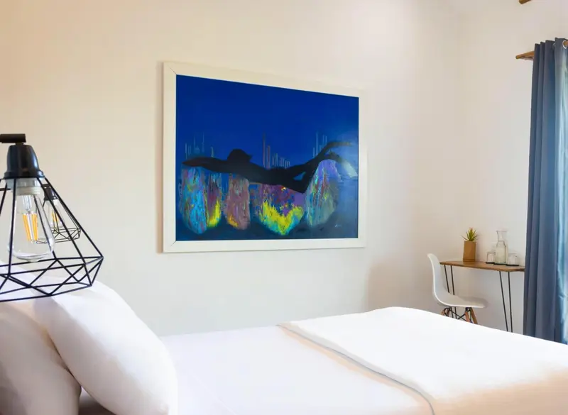 Une chambre lumineuse avec un lit blanc et une décoration murale abstraite.